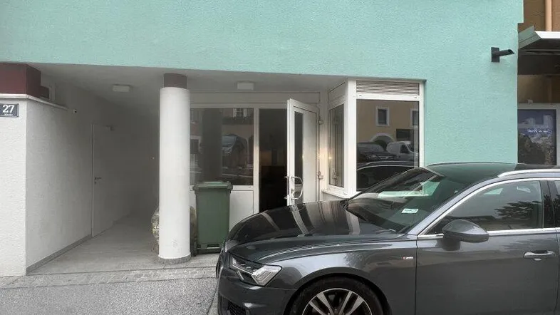 Die moderne Fassade des Gebäudes in Mintgrün mit Eingangsbereich und einem geparkten Auto davor.