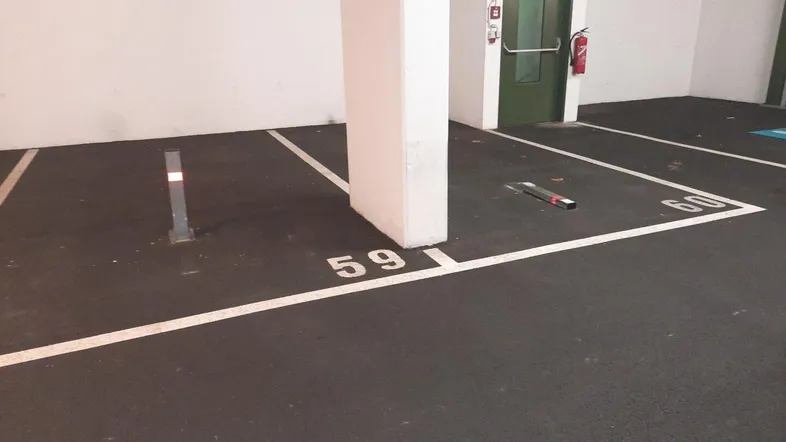 Tiefgaragenstellplatz Nummer 59 mit Säule, Notausgang und Feuerlöscher in einer gut beleuchteten Umgebung.