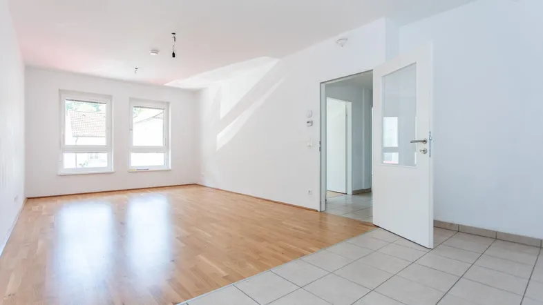 Helles, leeres Wohnzimmer mit Parkettboden und Fliesen im Eingangsbereich, bereit zur individuellen Gestaltung.