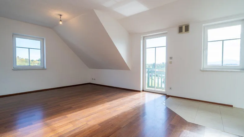 Helles Zimmer im Dachgeschoss mit Holzboden, Zugang zum Balkon und schrägen Wänden.