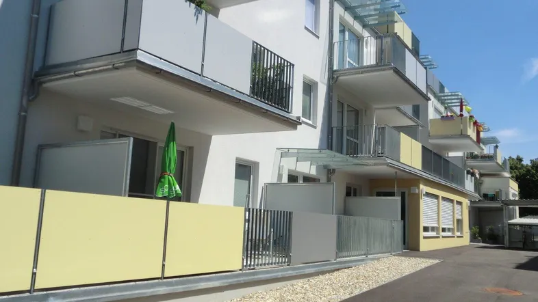 Moderne Wohnanlage mit hellen Fassaden, Balkonen und Kiesflächen im Außenbereich.