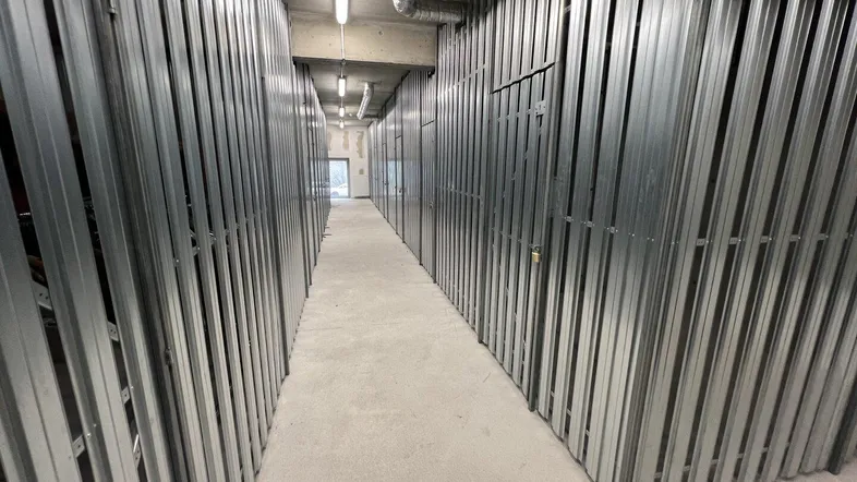 Langer Gang mit zahlreichen Metall-Lagereinheiten und Betonboden, beleuchtet von Deckenleuchten.
