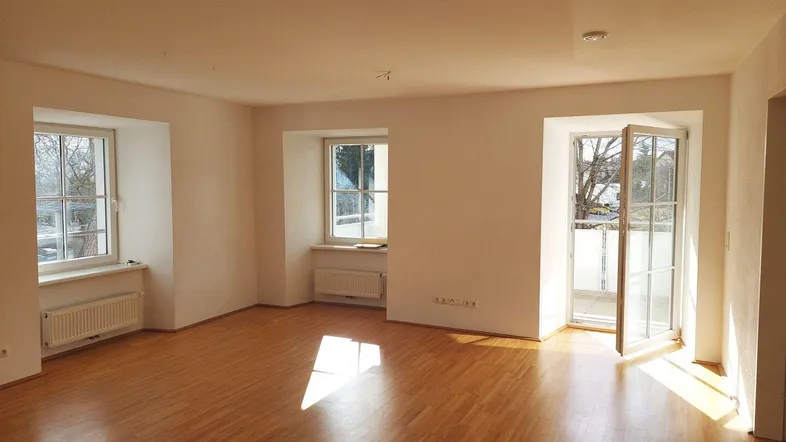 Helles, leeres Wohnzimmer mit Parkettboden und Zugang zu einem französischen Balkon.