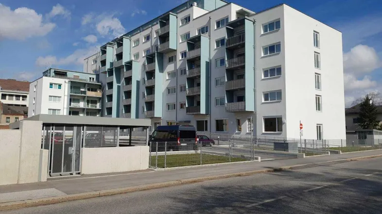 Modernes Mehrfamilienhaus mit weißer Fassade, blauen Akzenten und zahlreichen Balkonen unter blauem Himmel.