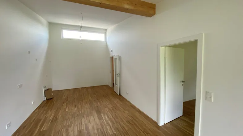 Heller Raum mit Holzbalken, Parkettboden und hoher Fensterfront, bereit für individuelle Gestaltung.