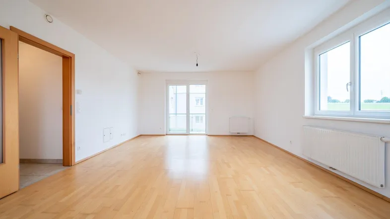 Helles Wohnzimmer mit Parkettboden, weißen Wänden und Zugang zum Balkon.