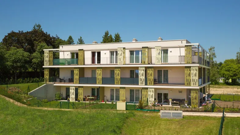 Modernes Mehrfamilienhaus mit Balkonen und grüner Umgebung unter blauem Himmel.