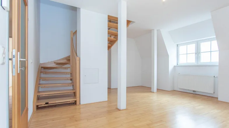 Helles, geräumiges Zimmer mit Parkettboden, Dachschrägen und einer Holztreppe, die in eine weitere Etage führt.