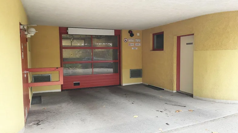 Eingangsbereich eines Gebäudes mit gelber Fassade, rotem Garagentor und separater Zugangstür.