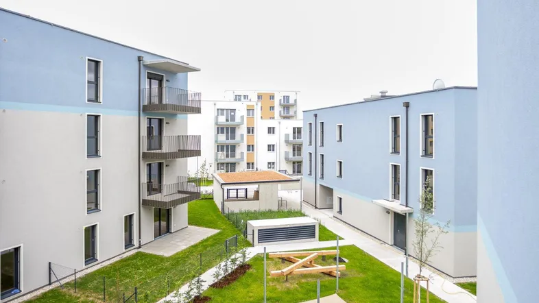 Moderne Wohngebäude mit hellblauen Fassaden, Balkonen und einer grünen Rasenfläche mit Spielgeräten.