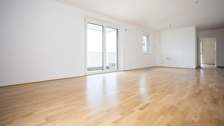 Helles, leeres Zimmer mit Parkettboden und Zugang zu einem Balkon, bereit zum Einrichten.