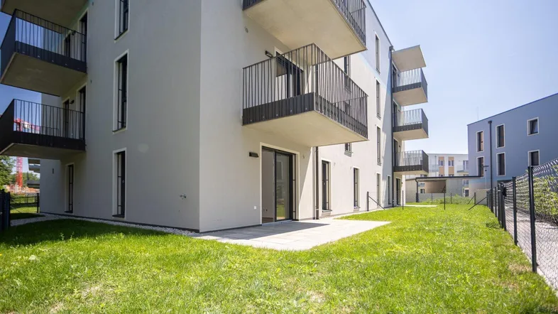 Moderne Wohnanlage mit Terrassenzugang und Grünfläche im Außenbereich unter blauem Himmel.