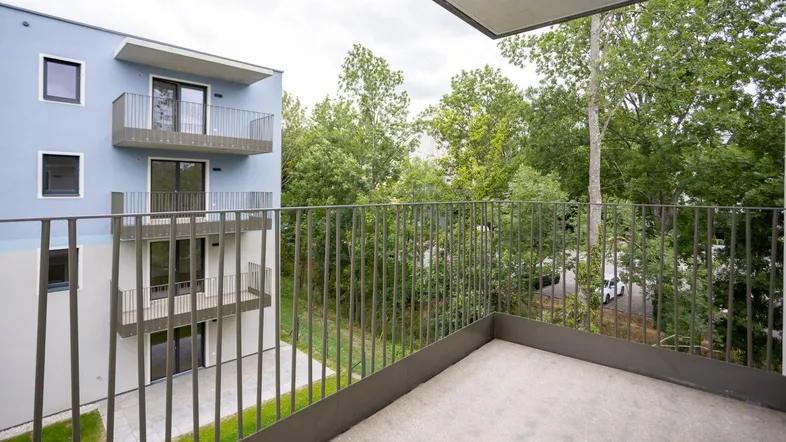 Geräumiger Balkon mit Blick ins Grüne und auf die moderne Gebäudefassade.