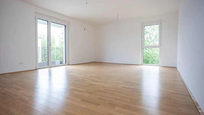 Helles, leeres Zimmer mit Parkettboden und Zugang zu einem Balkon.
