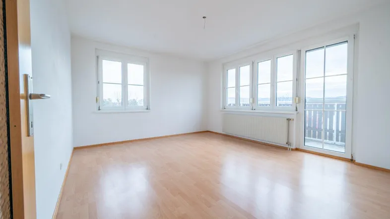 Heller Raum mit Laminatboden, großen Fenstern und Zugang zu einem Balkon.