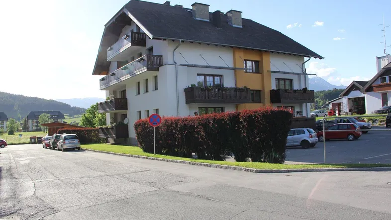 Mehrfamilienhaus mit mehreren Balkonen und Satteldach in ländlicher Umgebung mit Parkplätzen.