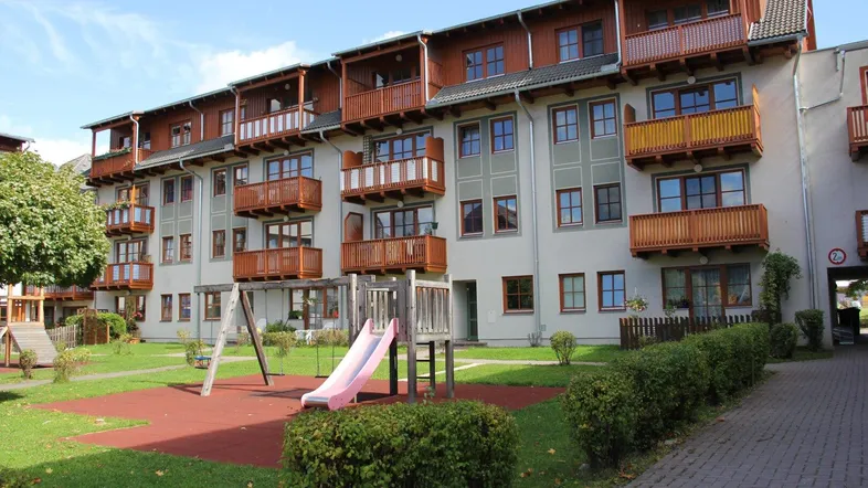 Modernes Mehrfamilienhaus mit zahlreichen Holz-Balkonen und einem Spielplatz im gemeinschaftlichen Gartenbereich.