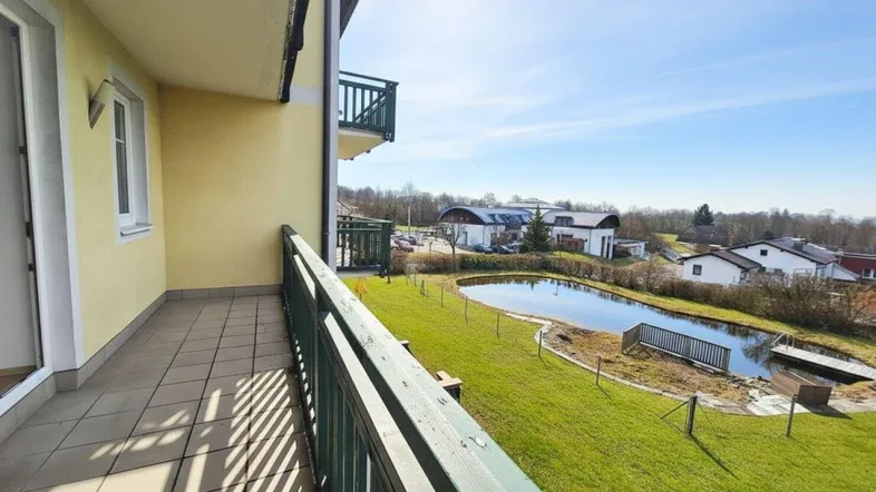 Heller Balkon mit Fliesenboden und weitem Blick auf einen Teich und die umliegende Landschaft.