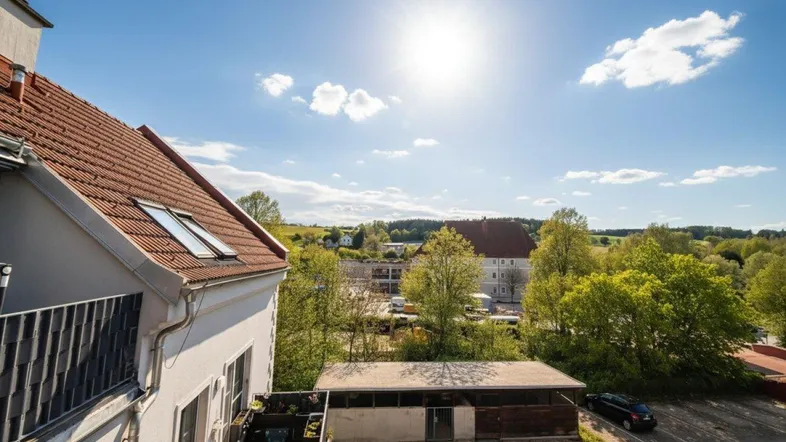Sonniger Ausblick von einem Balkon auf die umliegende Landschaft und weitere Gebäude.