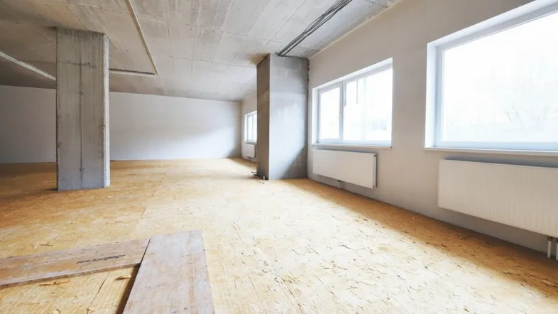Großer, heller Innenraum im Rohbauzustand mit großen Fenstern und OSB-Plattenboden.