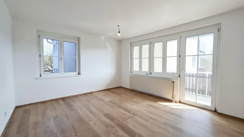 Helles, leeres Zimmer mit Laminatboden und Zugang zu einem Balkon, ideal als Wohnzimmer.