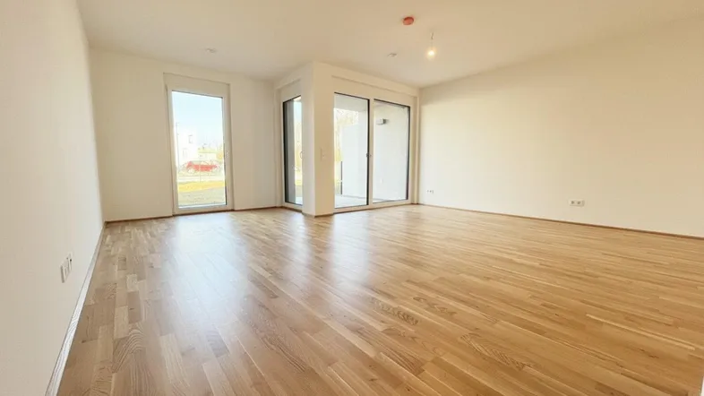 Helles und geräumiges Wohnzimmer mit neuem Parkettboden und großen Fenstern zum Außenbereich.