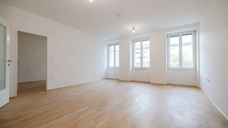 Helles, leeres Zimmer mit Parkettboden und mehreren Fenstern, bereit zur individuellen Gestaltung.