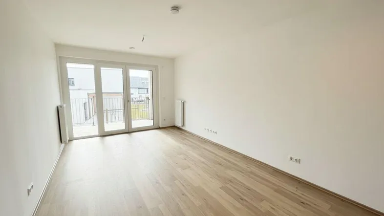 Helles Zimmer mit Holzboden und Zugang zu einem Balkon, ideal als Wohn- oder Schlafzimmer.