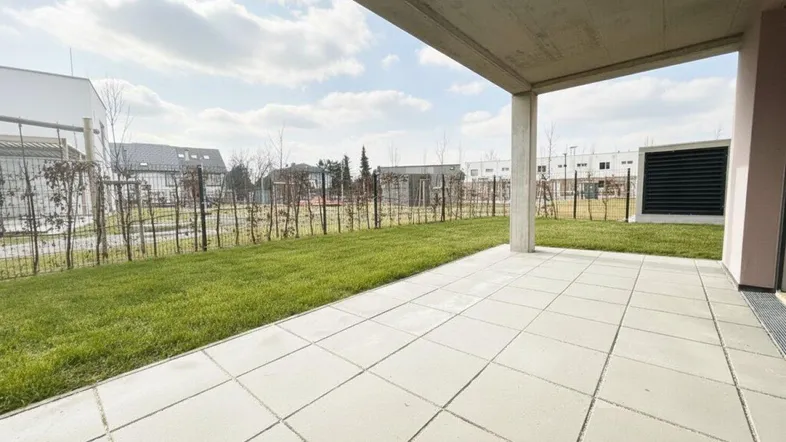 Geräumige Terrasse mit Fliesenboden und angrenzender Rasenfläche, ideal für Entspannung im Freien.