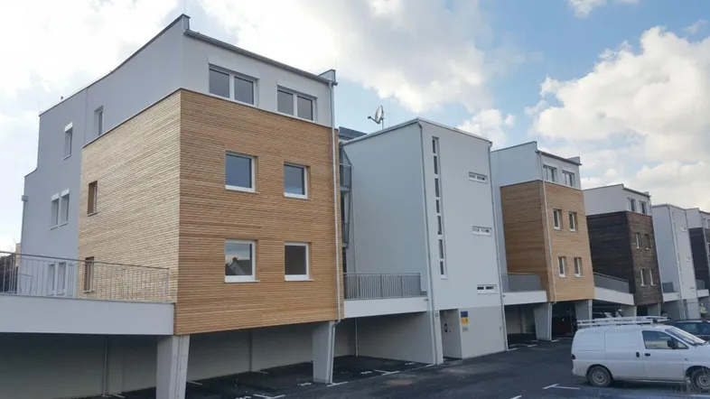 Moderne Wohnanlage mit Holzfassadenelementen und überdachten Parkplätzen im Erdgeschoss.