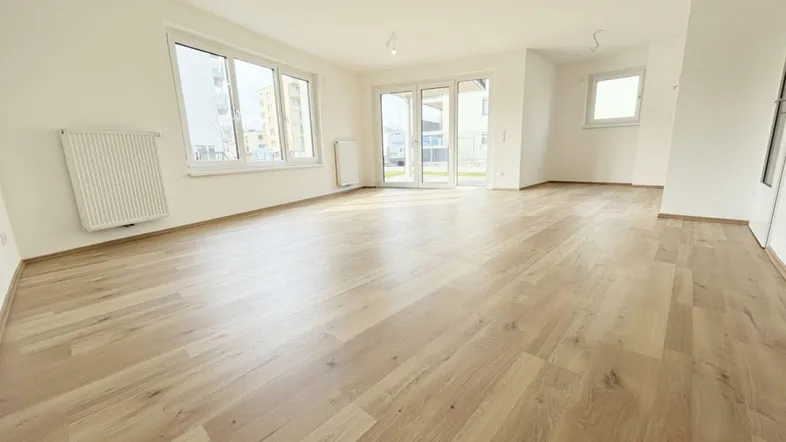 Helles, leeres Wohnzimmer mit großen Fenstern, Laminatboden und Zugang zur Terrasse.