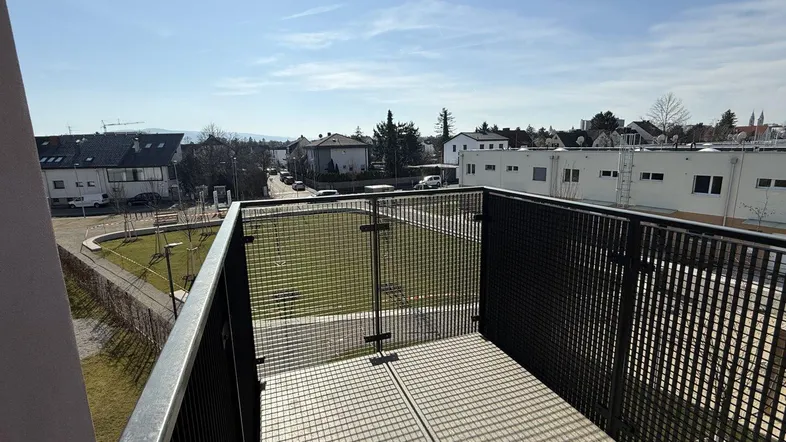 Heller Balkon mit Metallgeländer und Blick auf die umliegende Wohngegend unter blauem Himmel.