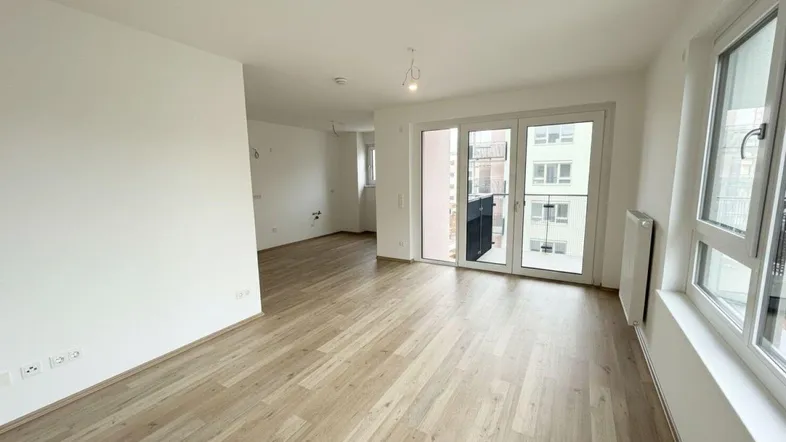 Helles, leeres Zimmer mit modernem Laminatboden und Zugang zu einem Balkon.