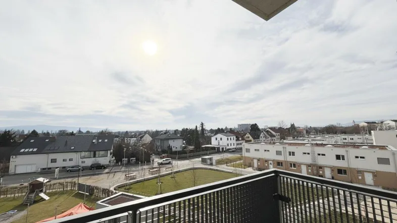 Blick vom Balkon auf die umliegende Wohngegend mit Grünflächen und weiteren Gebäuden.