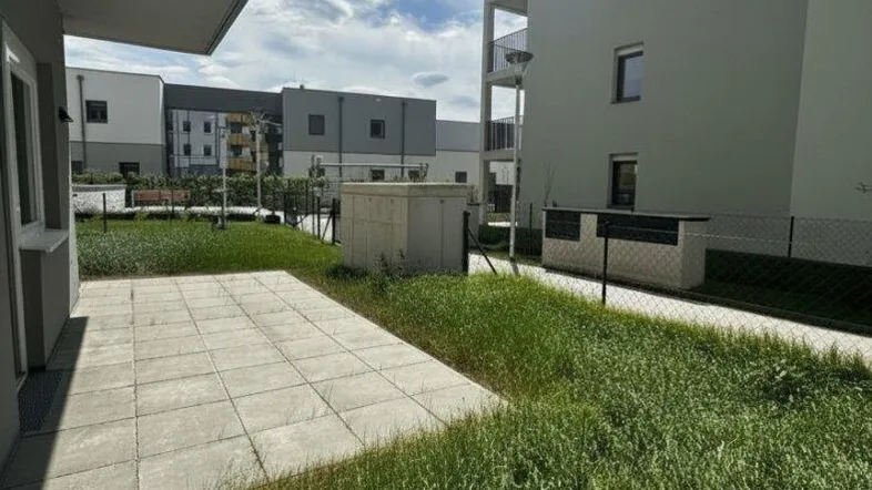 Terrasse mit Rasenfläche vor einem modernen Wohngebäude unter blauem Himmel.