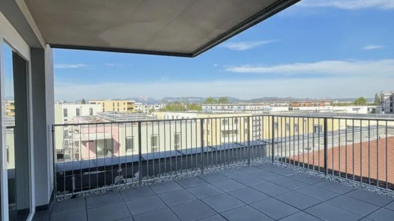 Geräumige Dachterrasse mit dunklen Fliesen, Metallgeländer und weitem Blick über die Stadt und Berge.