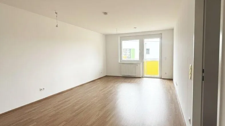 Helles, leeres Wohnzimmer mit modernem Laminatboden und Zugang zum Balkon.