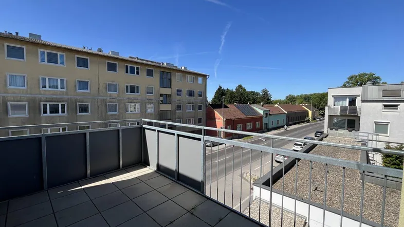 Geräumiger Balkon mit Fliesenboden und Blick auf die umliegenden Gebäude und die Straße.