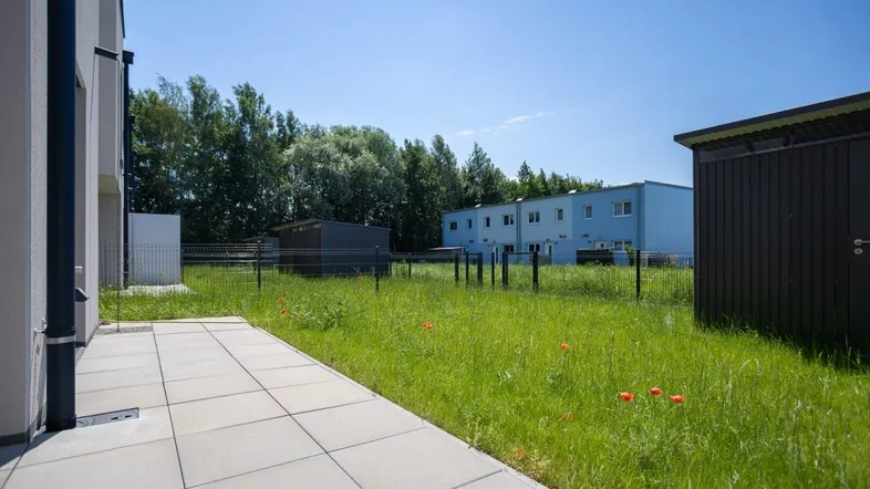 Große gepflasterte Terrasse mit Blick auf eine grüne Wiese und weitere Gebäude unter blauem Himmel.