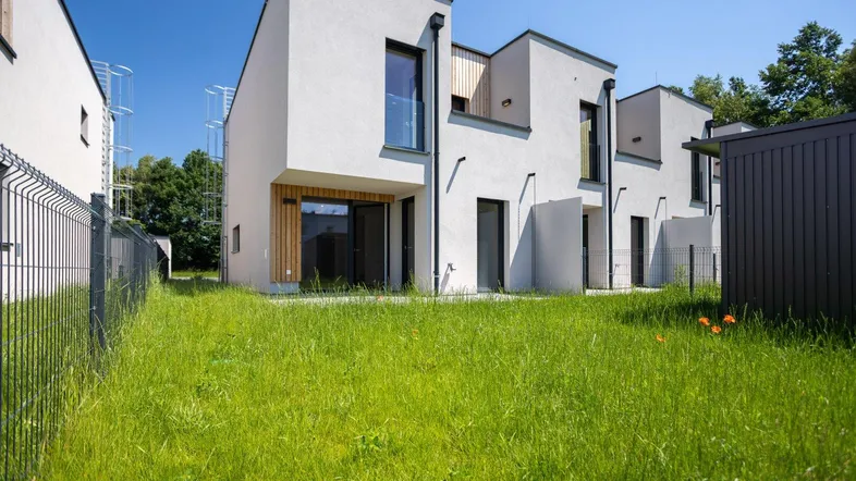 Moderne Reihenhäuser mit weißer Fassade und Holzdetails, umgeben von einer grünen Rasenfläche unter blauem Himmel.