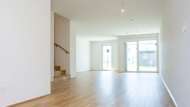 Helles, offenes Wohnzimmer mit Parkettboden und Zugang zu großen Fenstern und einer Treppe.