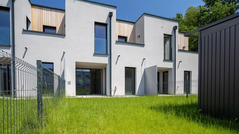 Moderne Reihenhäuser mit weißer Fassade, Holzdetails und privatem Gartenbereich.