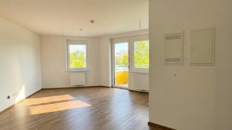 Heller, leerer Wohnbereich mit hochwertigem Parkettboden und Zugang zu einem sonnigen Balkon.
