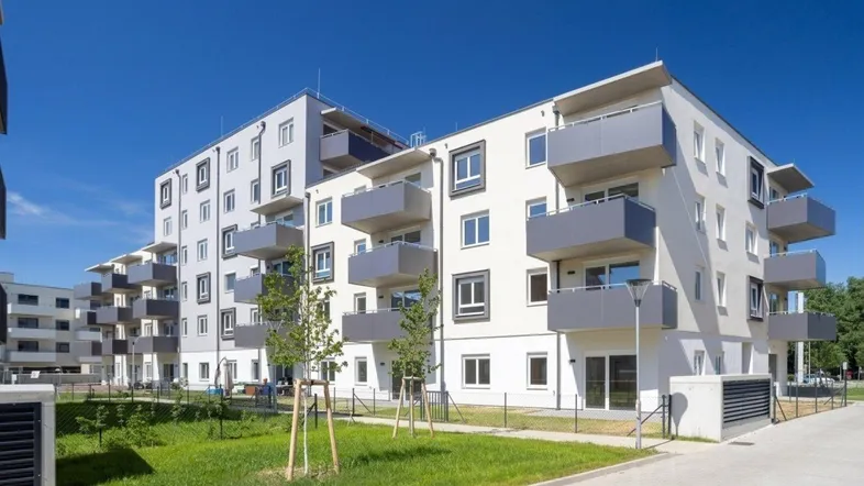 Modernes Mehrfamilienhaus mit weißer und grauer Fassade, Balkonen und gepflegten Grünflächen unter blauem Himmel.