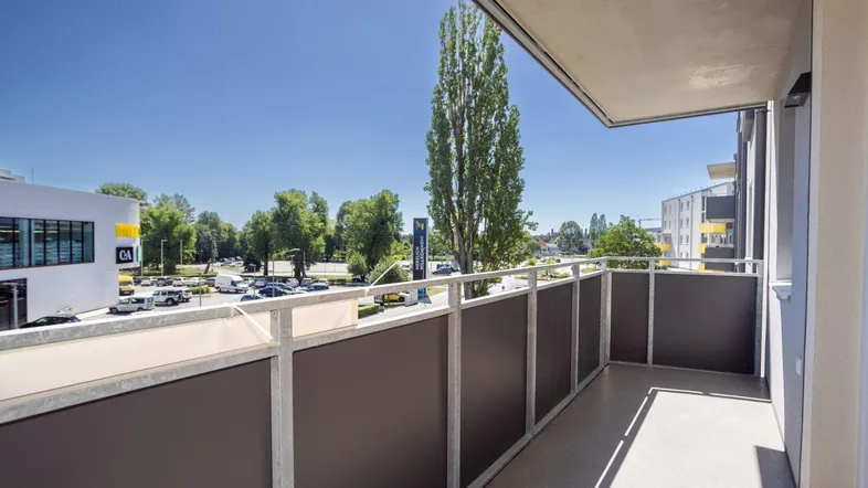 Langer Balkon mit Blick auf die Straße und umliegende Gebäude unter blauem Himmel.