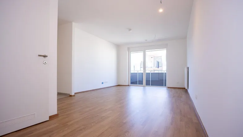Helles, leeres Zimmer mit Laminatboden und Zugang zu einem Balkon, ideal als Wohnbereich.