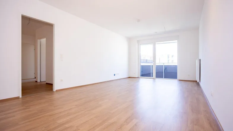 Helles, leeres Zimmer mit Laminatboden und Zugang zu einem Balkon, ideal als Wohnbereich.