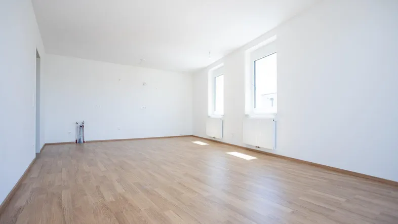 Heller, leerer Raum mit Laminatboden, weißen Wänden und zwei Fenstern, vorbereitet für eine Küche.