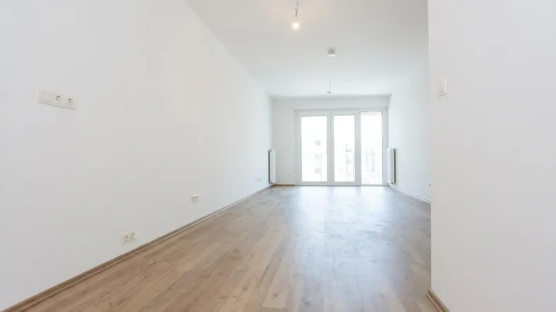Helles, unmöbliertes Wohnzimmer mit Laminatboden und Zugang zu einem großen Balkon.