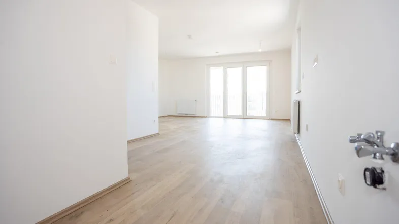 Geräumiger, heller Wohnbereich mit Laminatboden und viel Tageslicht durch die Balkontür.